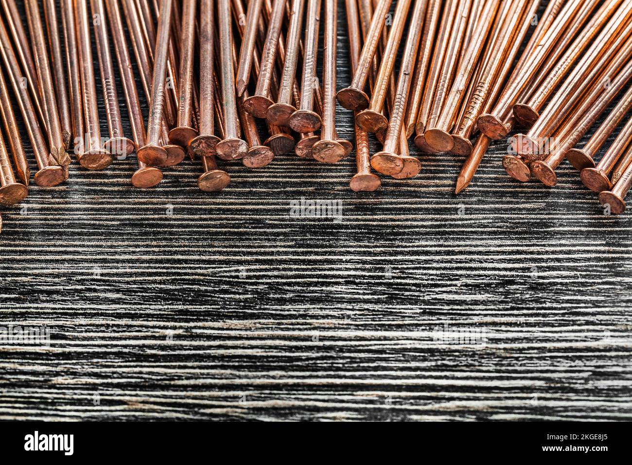 Heap of copper nails on wooden board. Stock Photo