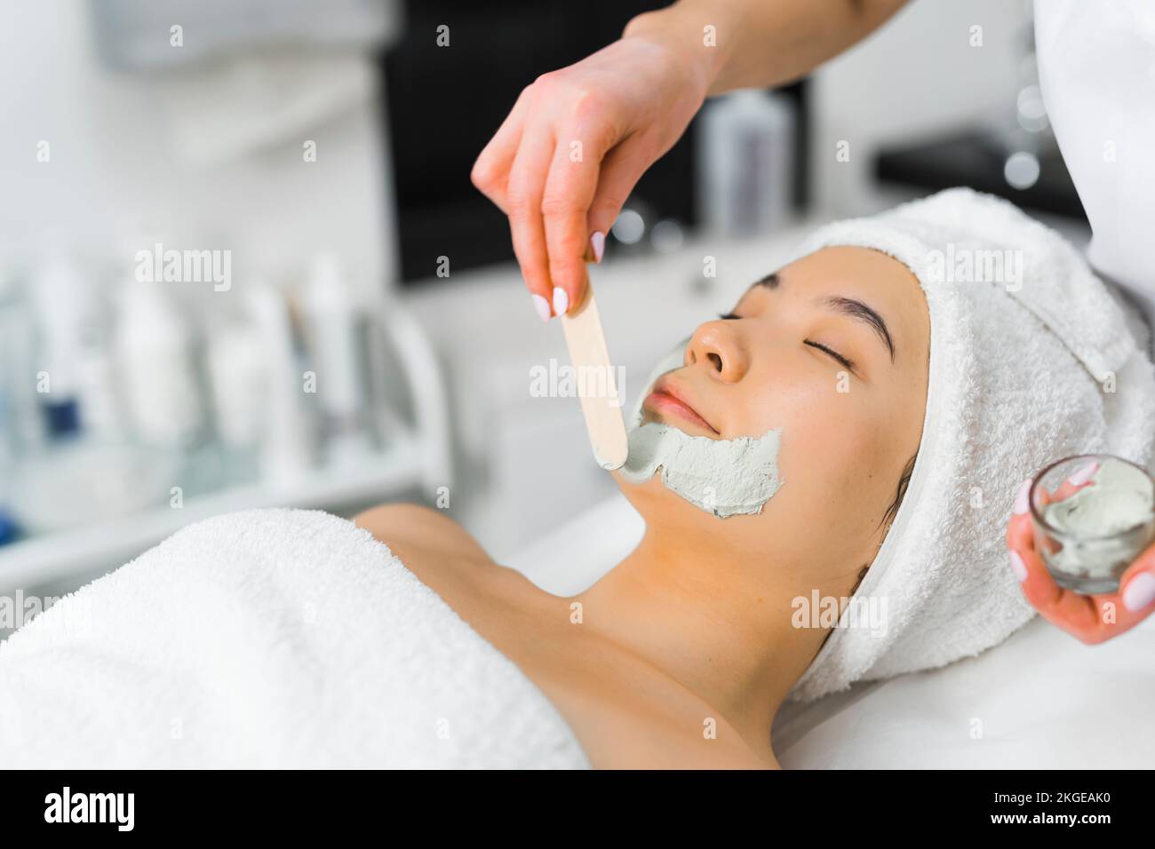 specialist putting a face mask on a client's face with a stick, side view medium closeup beauty center. High quality photo Stock Photo