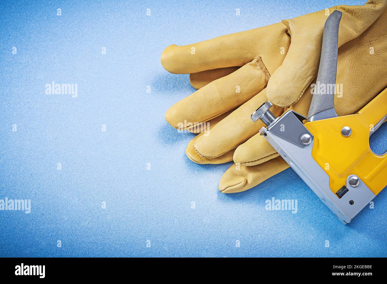 Leather protective gloves staple gun on blue background construction concept. Stock Photo