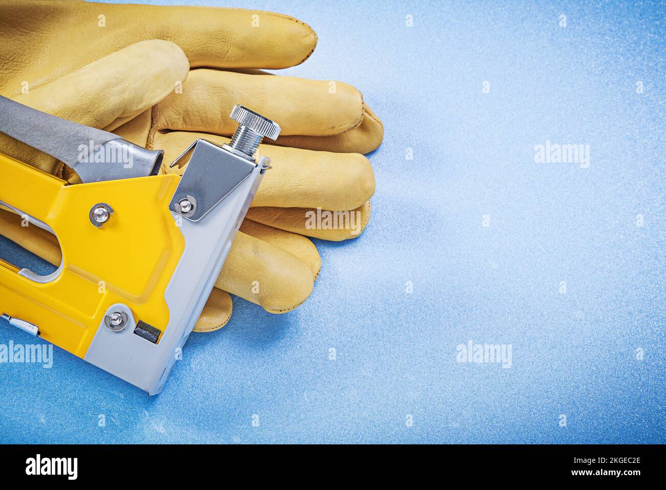 Leather safety gloves yellow construction stapler on blue background. Stock Photo
