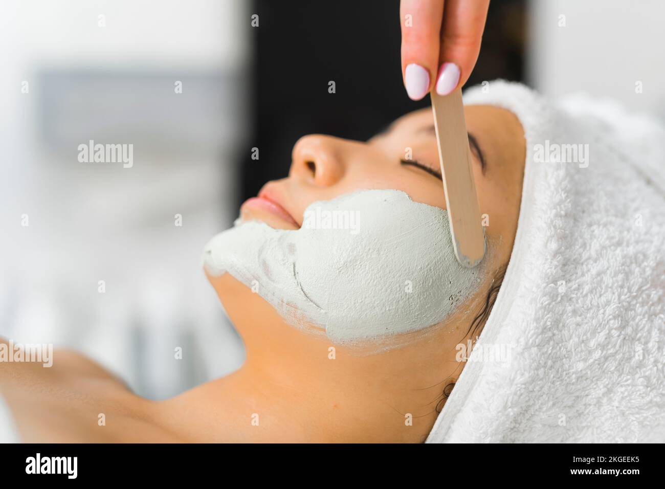 closeup side shot of a young Asian woman lying on a table relaxed and a professional making a face mask for her, cosmetology center. High quality photo Stock Photo