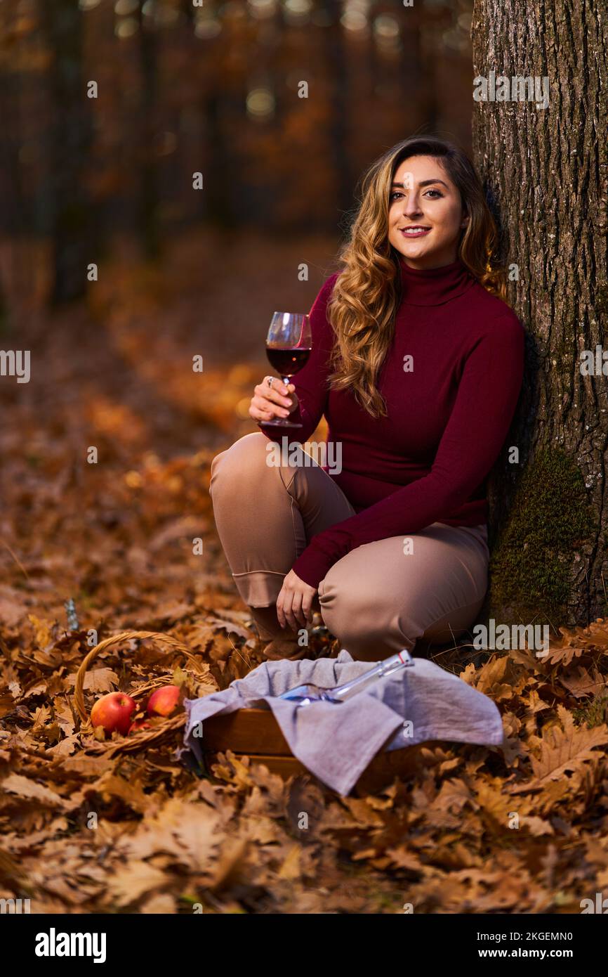 Beautiful plus size young indian woman enjoying a glass of red wine in the oak forest at sunset Stock Photo