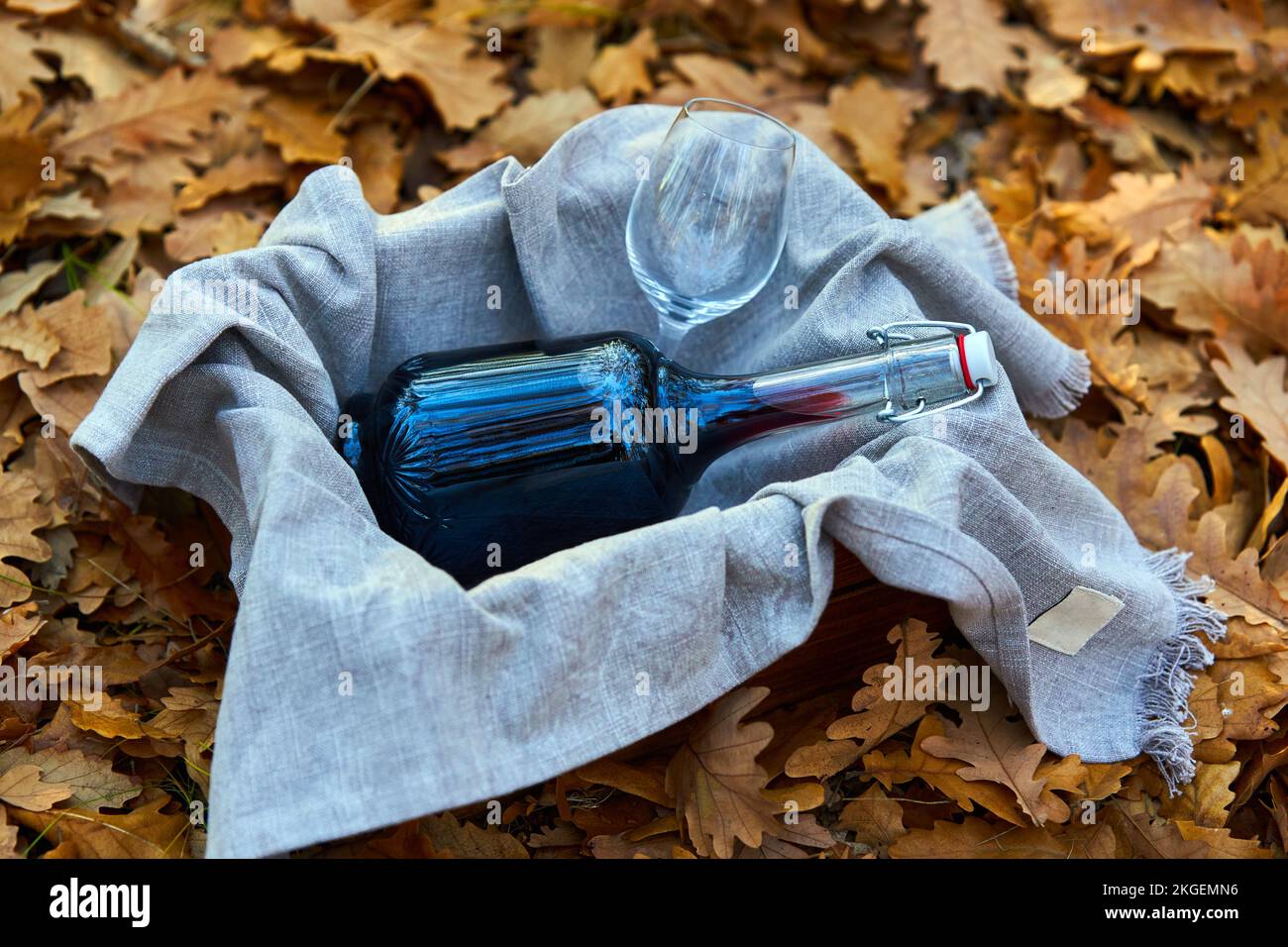 A bottle of red wine in a crate and a towel on the fallen leaves in the forest Stock Photo