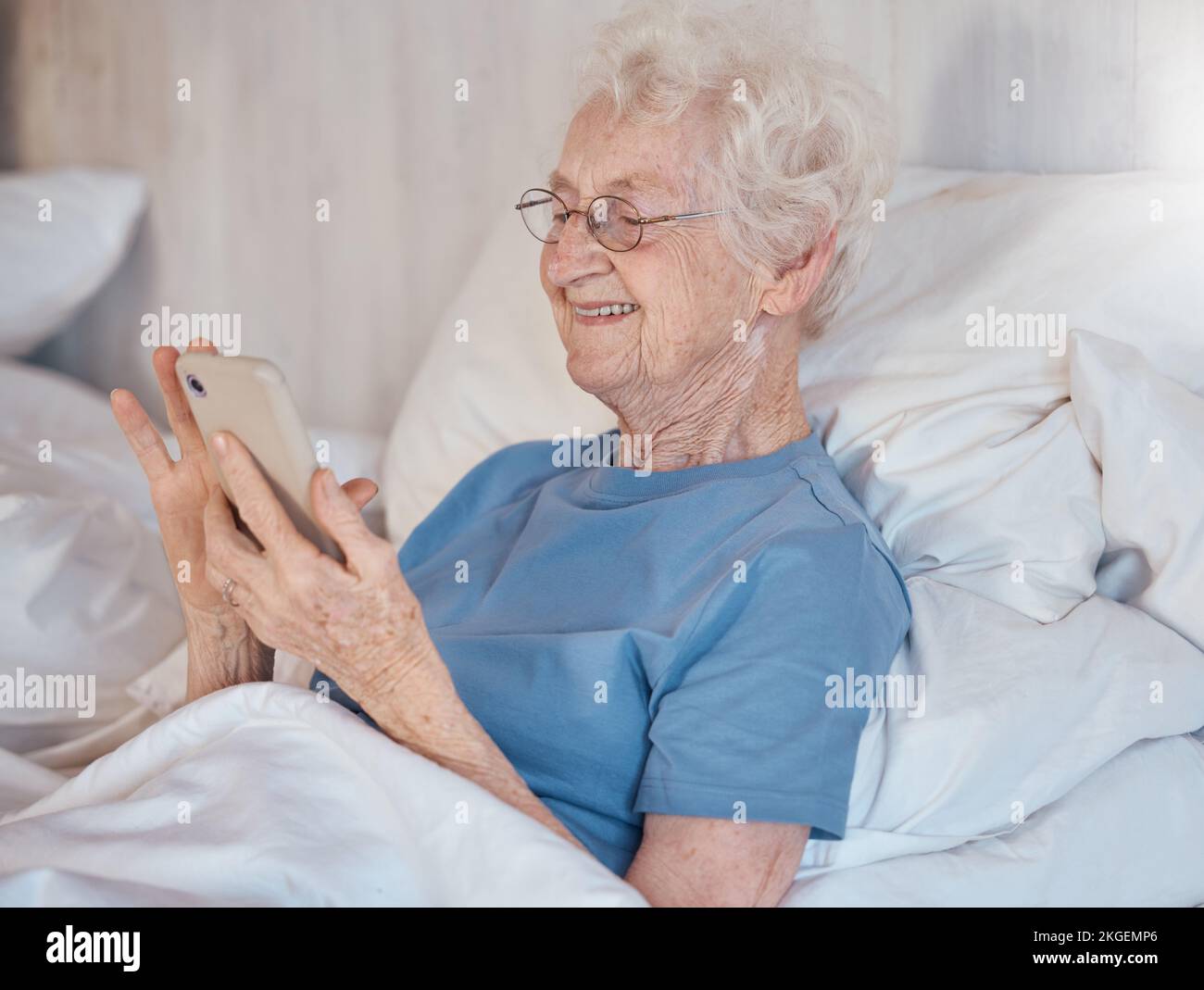 Elderly woman, retirement home and smartphone in bed of nursing home for medical care to relax to support healthcare. Senior with happy smile, in Stock Photo