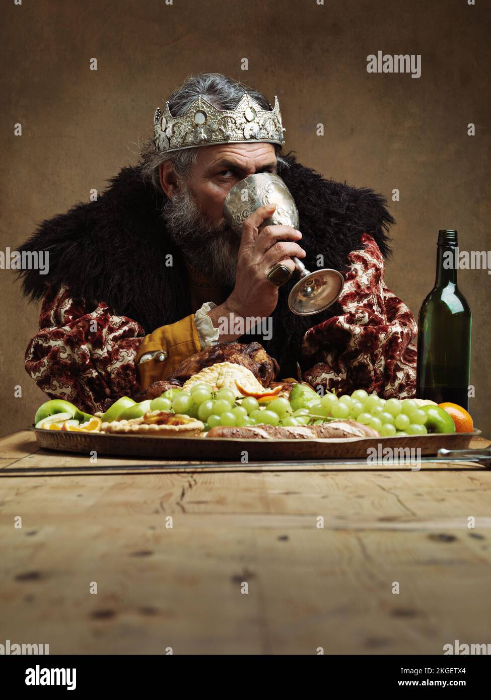 Drink deep to ease the woes of rule. A mature king feasting alone in a banquet hall. Stock Photo