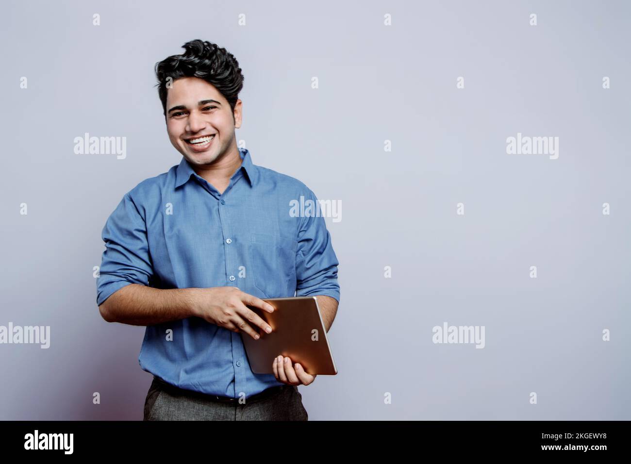 An Indian guy cant stop laughing hysterically over a joke, laughing out loud holding digital tablet and looking at the camera. comedian colleagues. Stock Photo