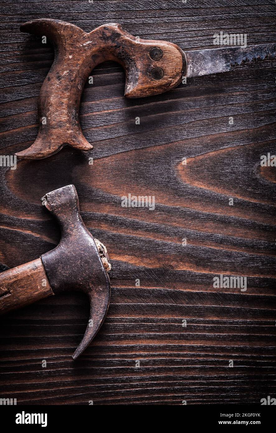 Rusty antique handsaw with claw hammer on vintage dark wooden