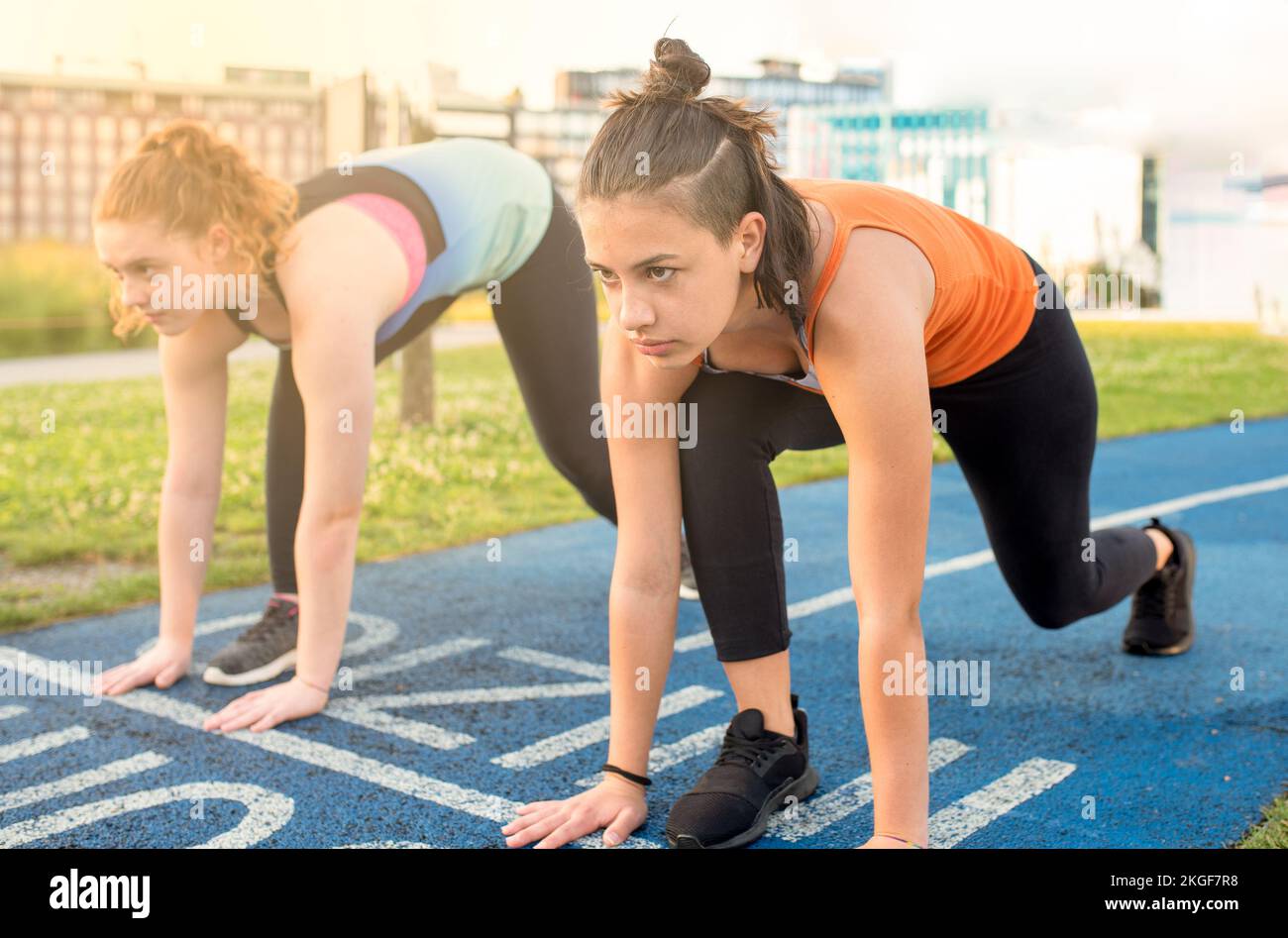 two young women on the start of a track for athletics 100 meters race, facial expression of determination and seriousness, healthy lifestyle Stock Photo
