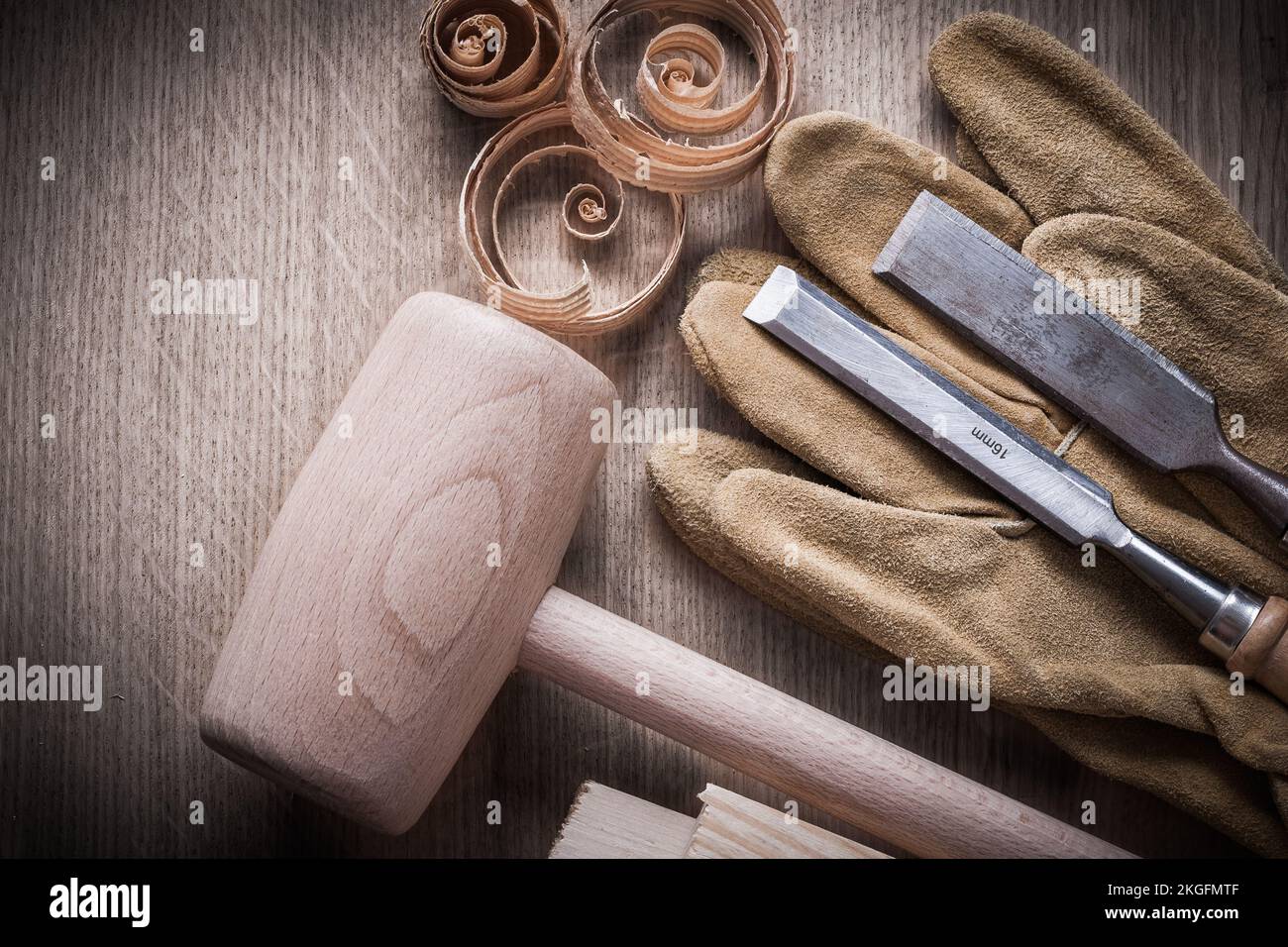 Wooden bricks hammer curled up planning chips firmer chisels leather gloves on wood board construction concept. Stock Photo