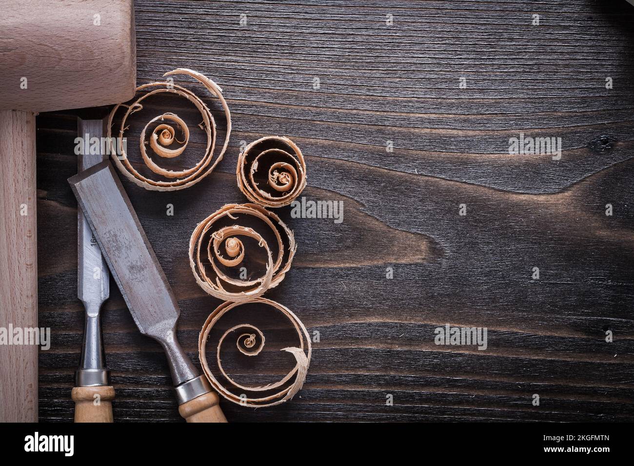 Wooden hammer flat chisels and curled up shavings on vintage wood board copy space image construction concept. Stock Photo