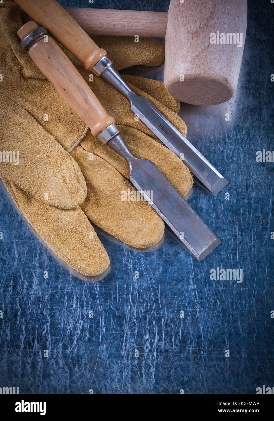 Wooden mallet firmer chisels and safety gloves on scratched metallic surface construction