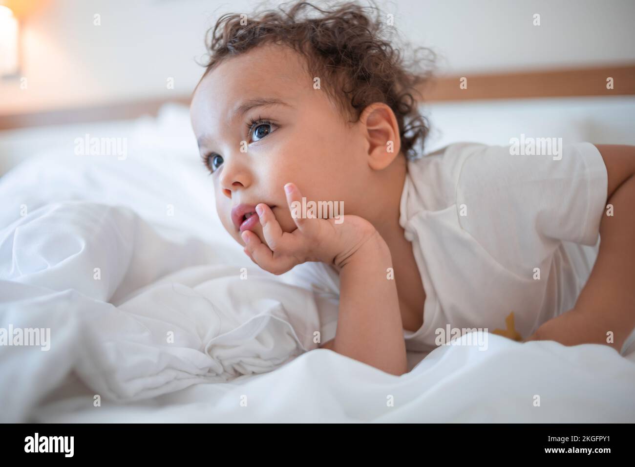 Little boy lies on his tummy on a white bed in the master bedroom Stock Photo