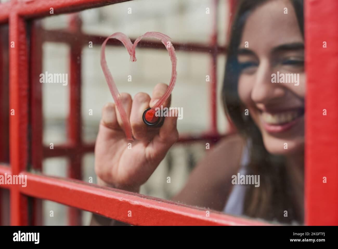 Woman, heart and drawing with lipstick in booth for love on travel vacation in London city. Happy, red cosmetics makeup and person graffiti on window Stock Photo