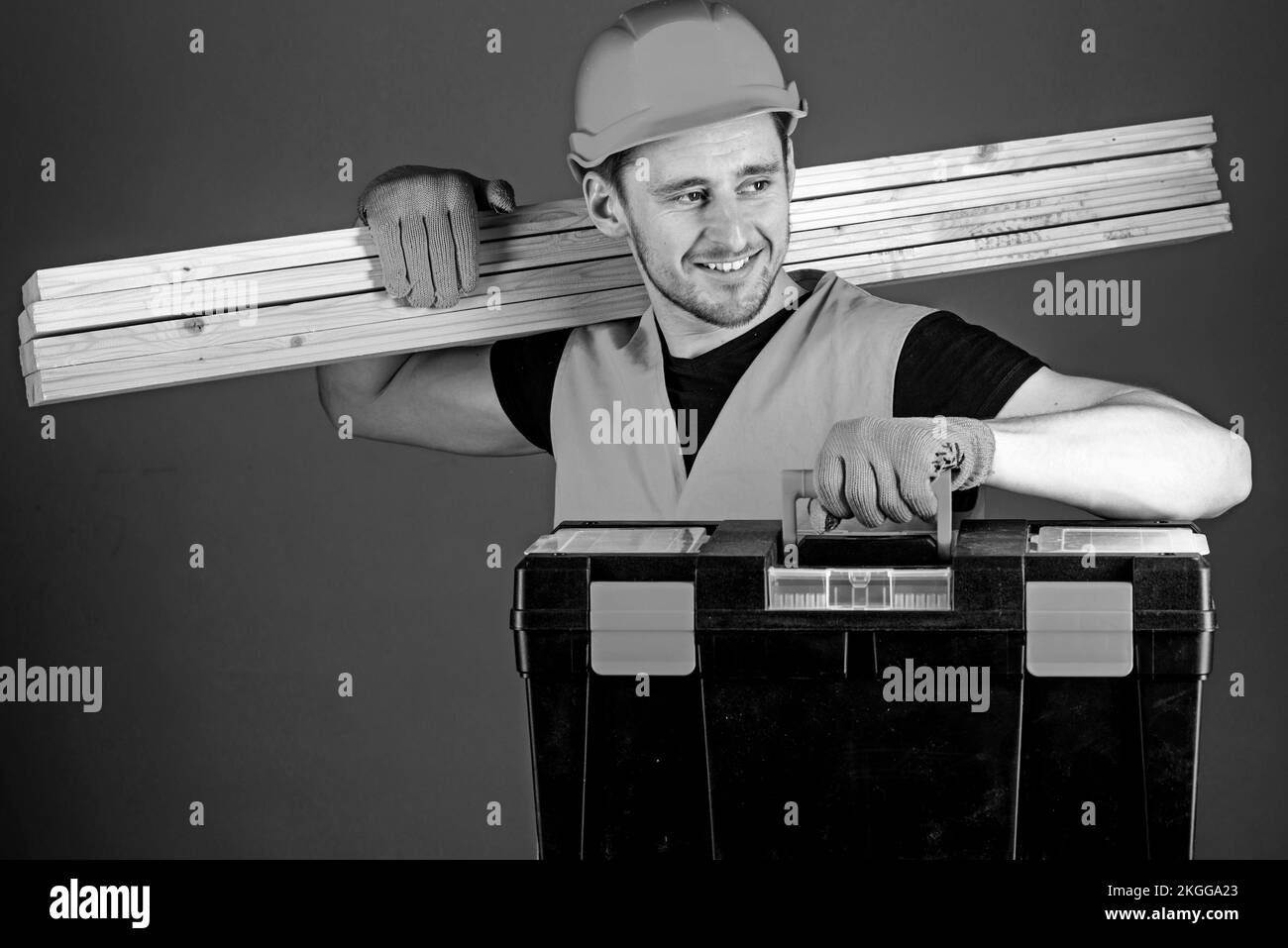 Man in helmet, hard hat holds toolbox and wooden beams, grey background. Professional woodworker