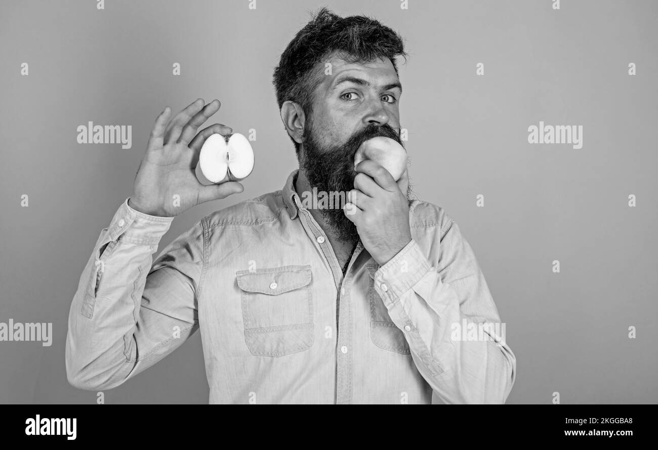 Man bearded eats fruit, holds apple blue background. Half of apple healthy lifestyle. Hipster demonstrates natural ecological apple. Nutritional value Stock Photo