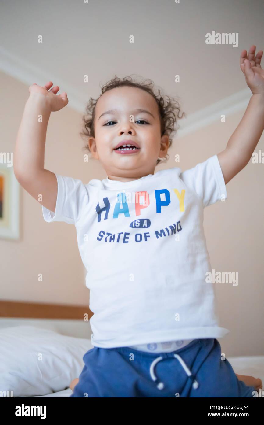 Funny happy kid jumping on parents bed in master bedroom Stock Photo
