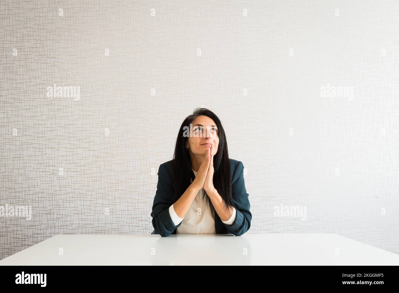 Young caucasian brunette business woman director in office pray for help hopeful in office behind desk for success and praise at work Stock Photo