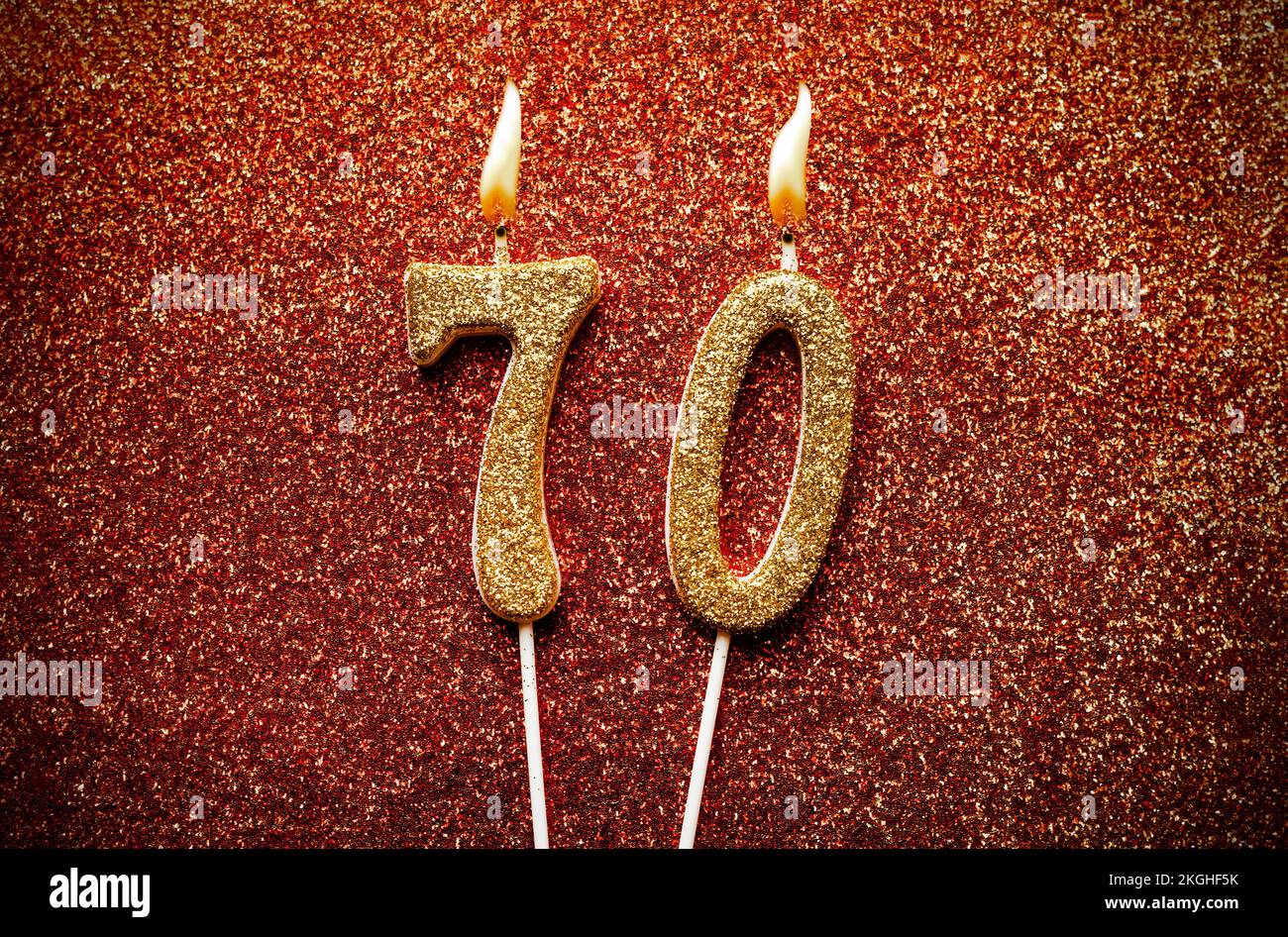 Burning golden color number 70 celebration candle on red glitter background Stock Photo