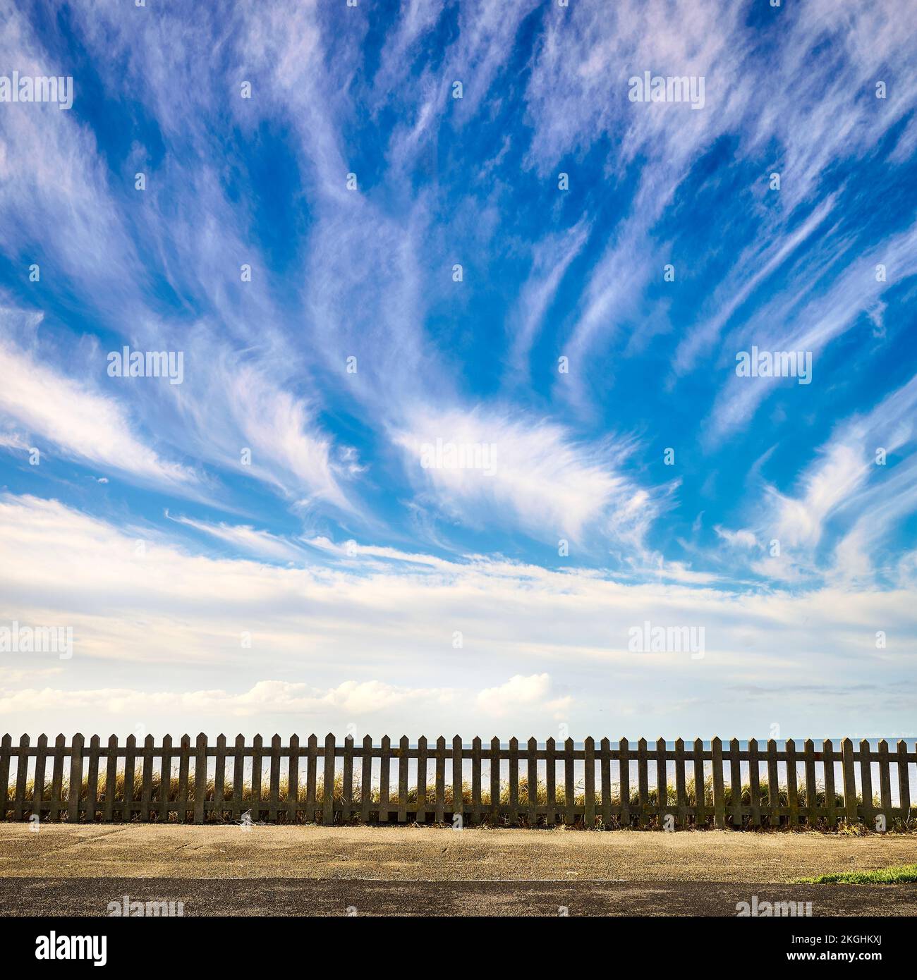 Regular concrete fence against blue sky and wispy cirrus clouds Stock Photo