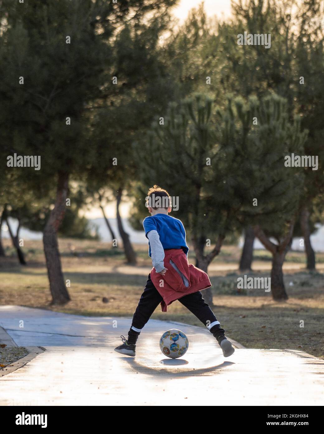 Rear view of boy playing with soccer ball between legs in nature