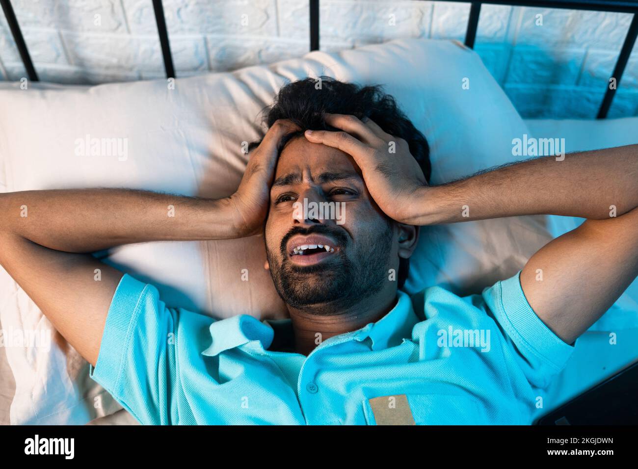 screaming young man suffering from sleeplessness or insomnia disorder at night on bedroom - concept of drug addict, migraine and stress Stock Photo