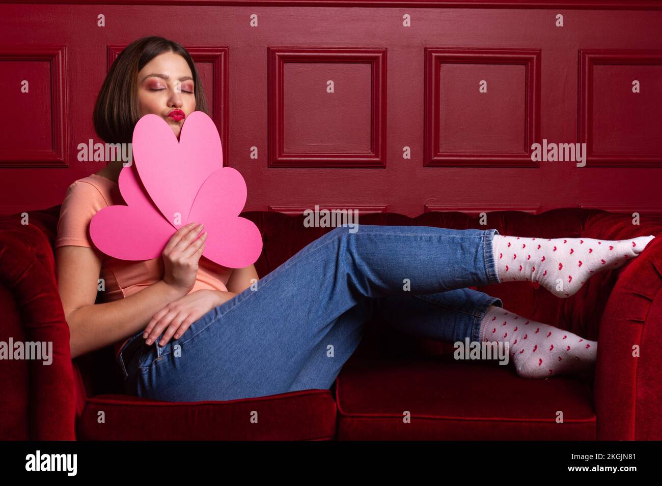 Women in jeans with closed eyes on a couch holding three heartshaped paper sheets and lips