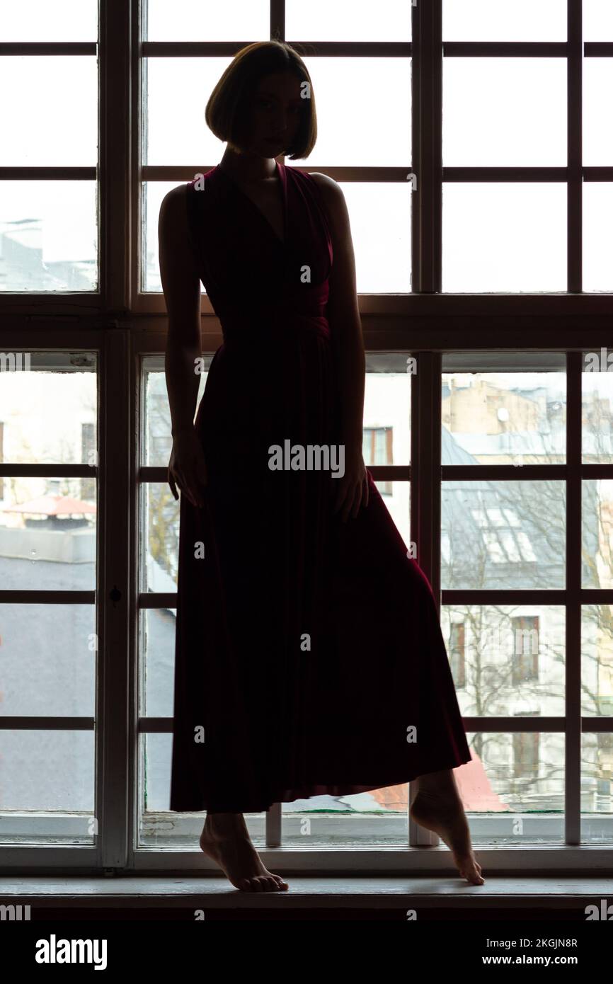 Silhouette of a woman in a red dress in front of a small pane window Stock Photo