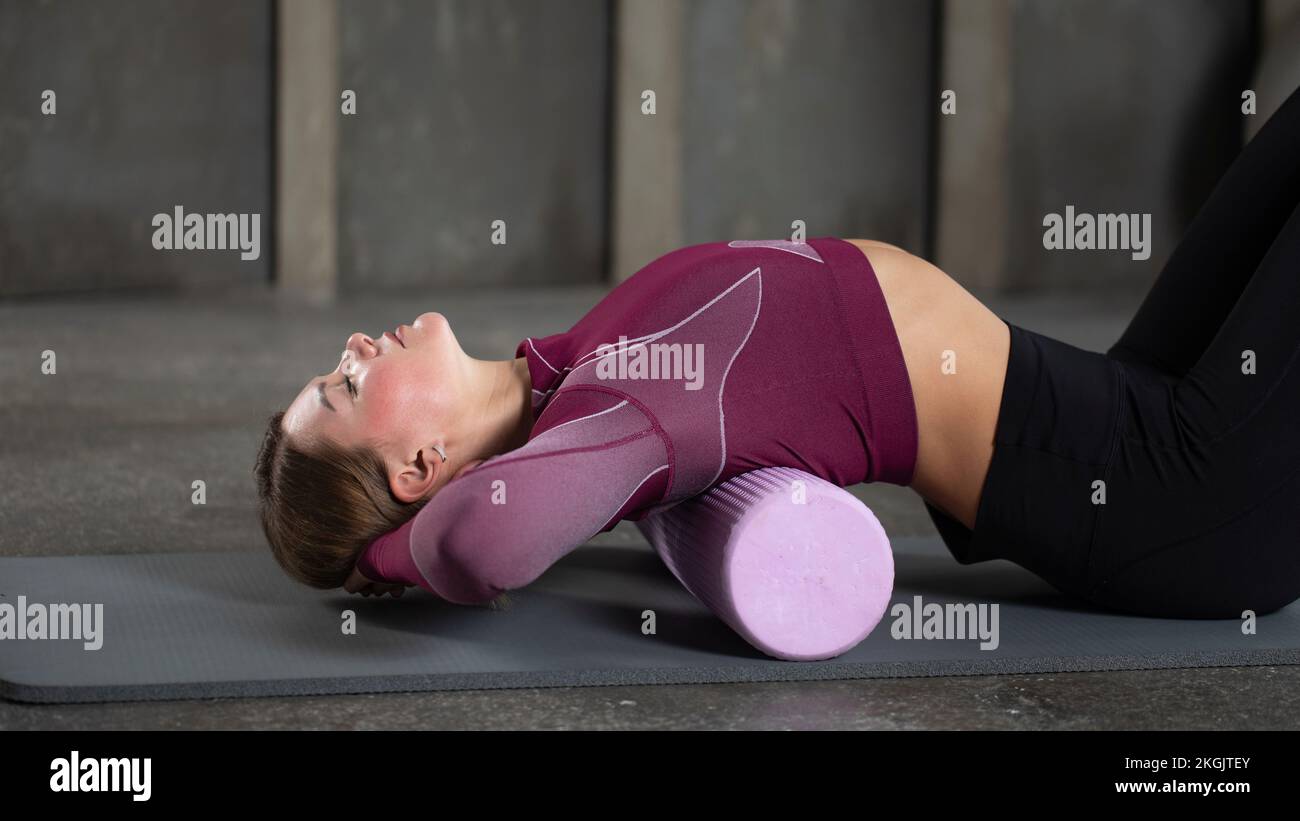 A woman performs a myofascial release for her back using a roll on a