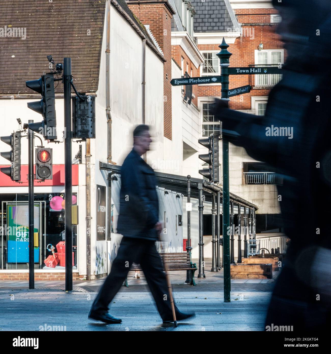 Epsom, Surrey, London UK, November 20 2022, Man Walking With A Walking Stick And Another Using A Mobile Phone Or Smart Phone On A Town Centre High Str Stock Photo