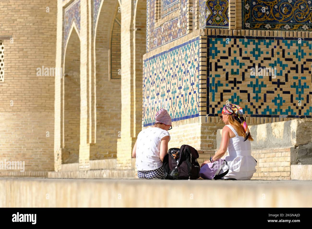 Bukhara Uzbekistan twofemale visitors rest outside the Mir-i Arab Madrasa and its ornate tile decoration - August 2022 Stock Photo