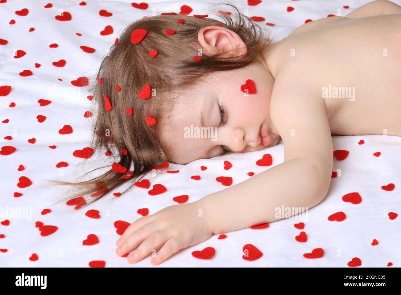 An infant sleeping with lots of red hearts surrounding him on white. Stock Photo