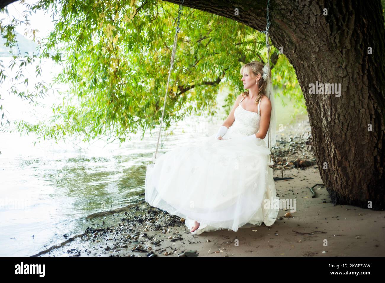Germany, Rhineland-Palatinate, portrait of pensive bride sitting on a swing at waterside of Rhine river Stock Photo