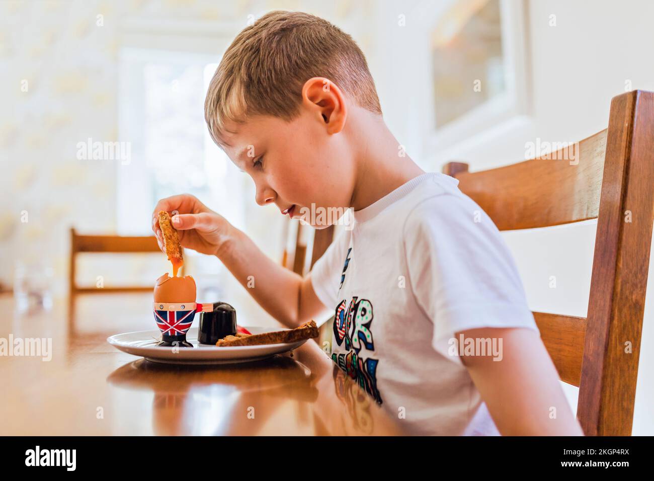 UK, sad boy sitting at breakfast table eating boiled egg Stock Photo