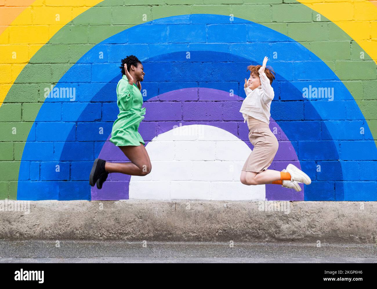 Happy female friends jumping in front of colorful wall Stock Photo - Alamy