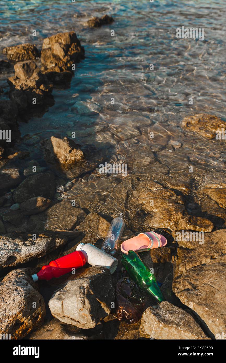 Empty plastic bottles and slippers floating on water at beach Stock Photo