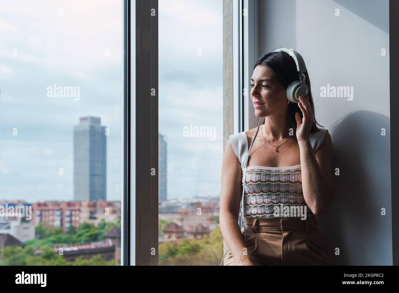 Young businesswoman listening to music on headphones by window at work place Stock Photo