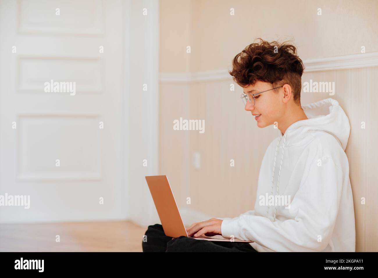 Smiling boy using laptop at home by wall Stock Photo
