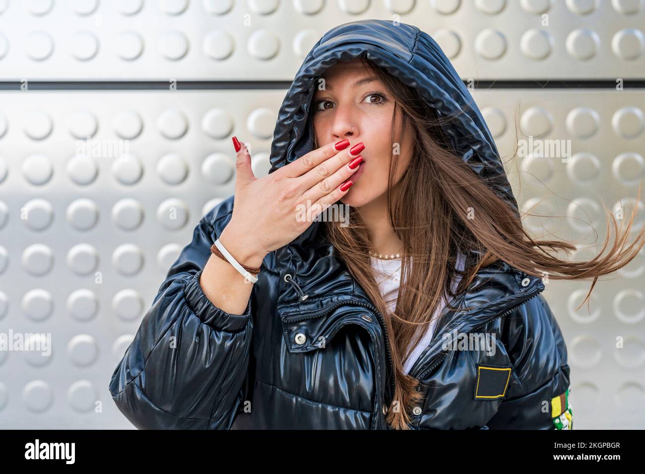 Woman covering mouth with hand in front of metal wall Stock Photo