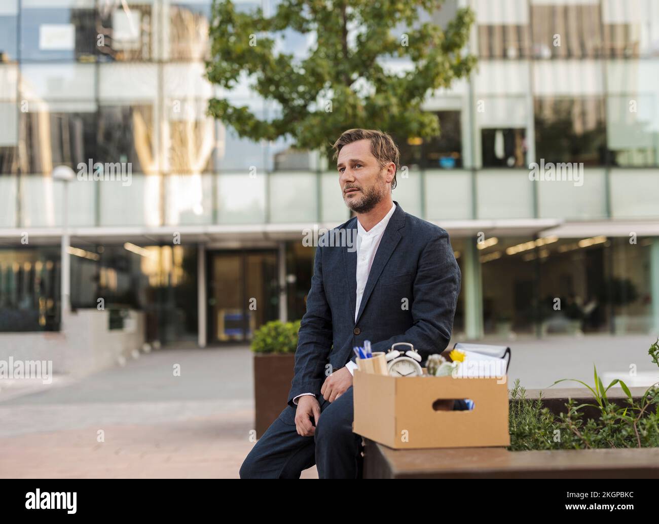 Sad businessman sitting with cardboard box outside office building Stock Photo