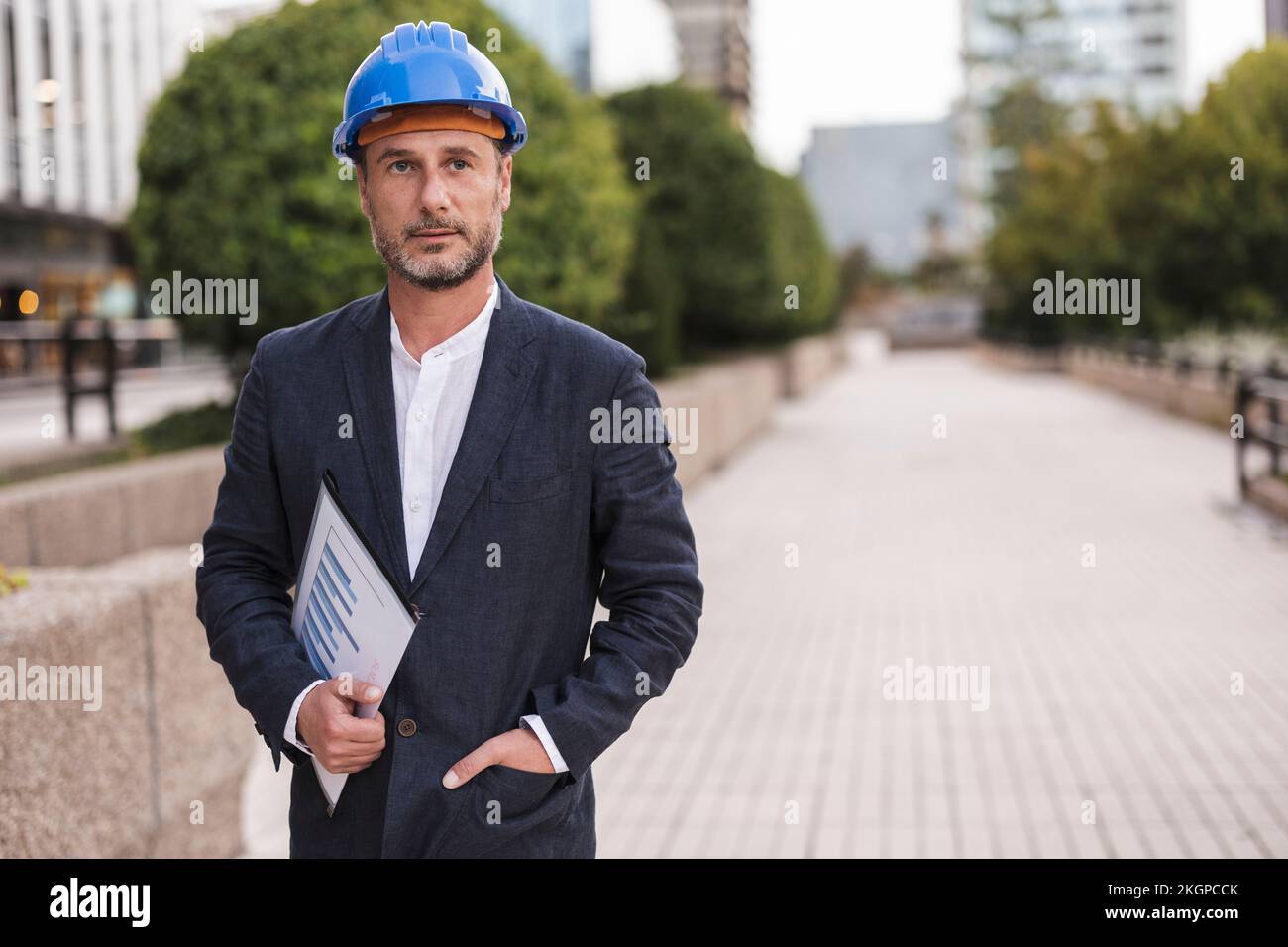 Contemplative engineer wearing hardhat standing at footpath Stock Photo