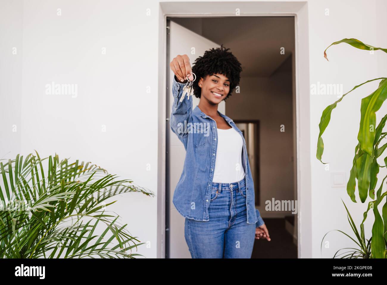 Happy young woman showing house keys standing in doorway Stock Photo ...