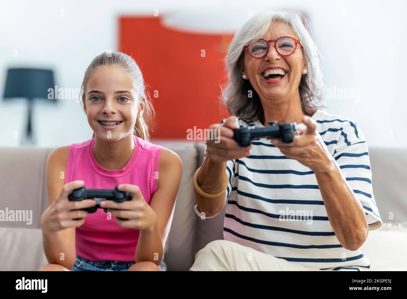 Happy grandmother and granddaughter playing video game with joysticks at home Stock Photo