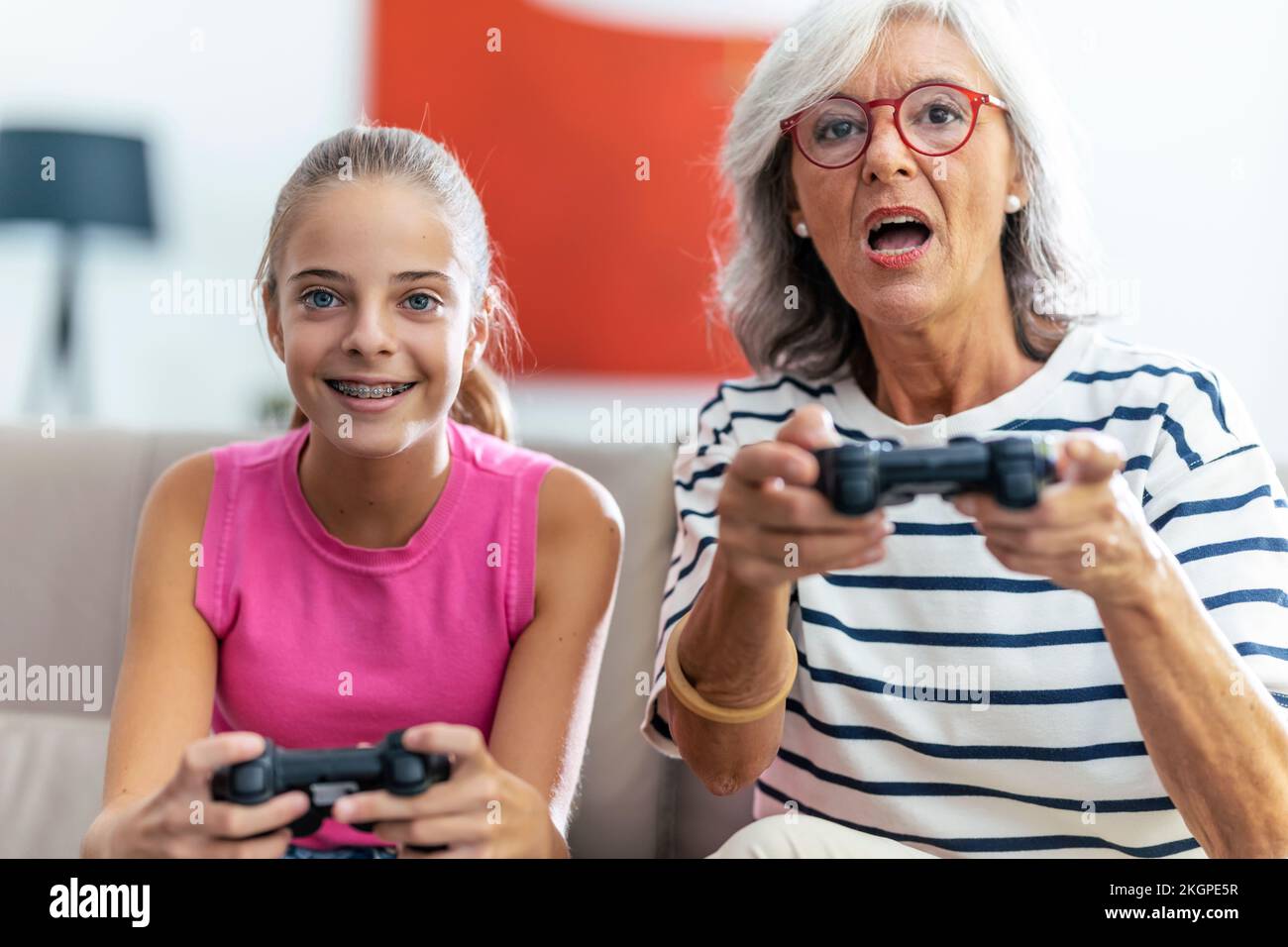 Concentrated grandmother and granddaughter playing video game with joysticks at home Stock Photo