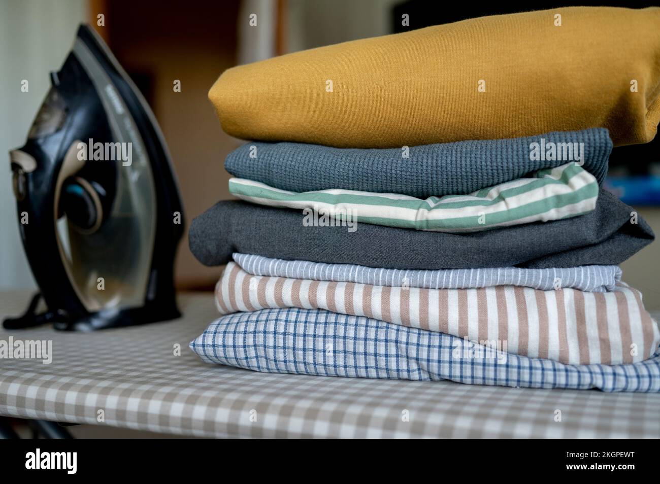 Iron by stack of clean clothes on ironing board at home Stock Photo