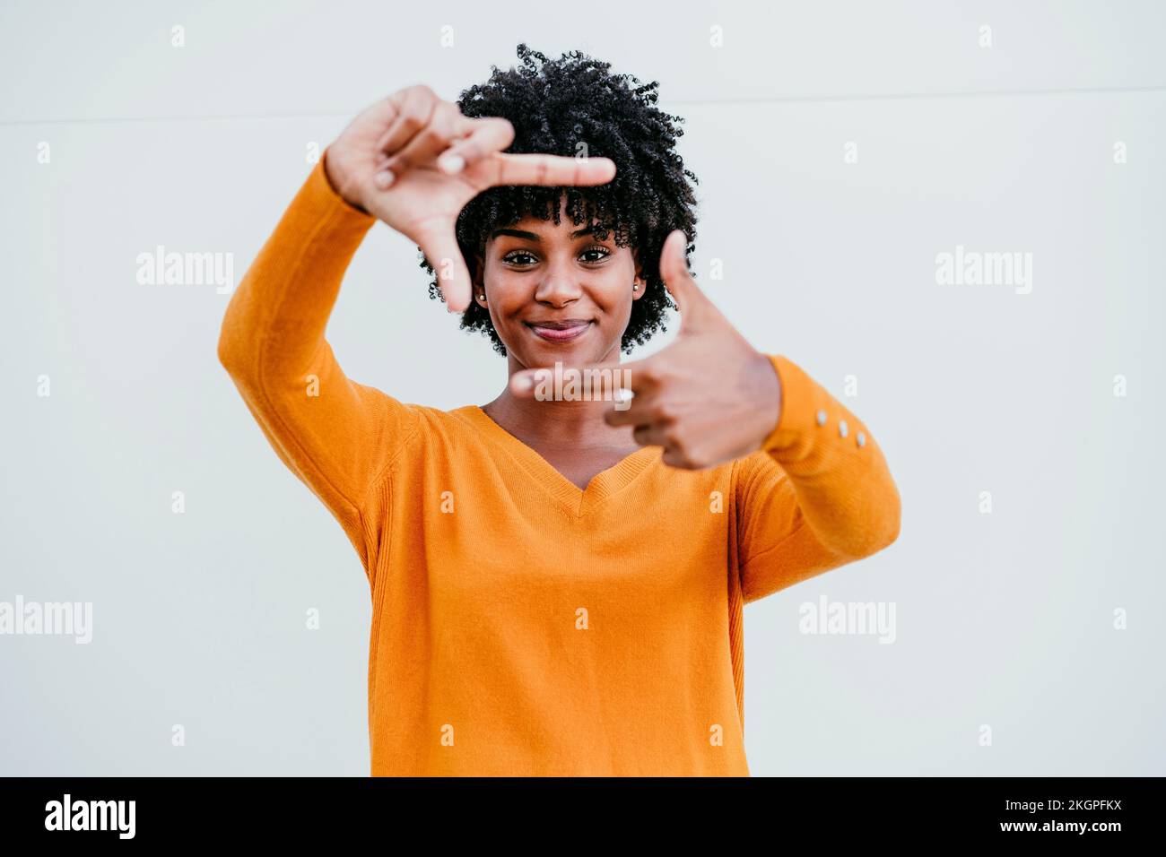 Smiling Afro woman making picture frame in front of wall Stock Photo ...