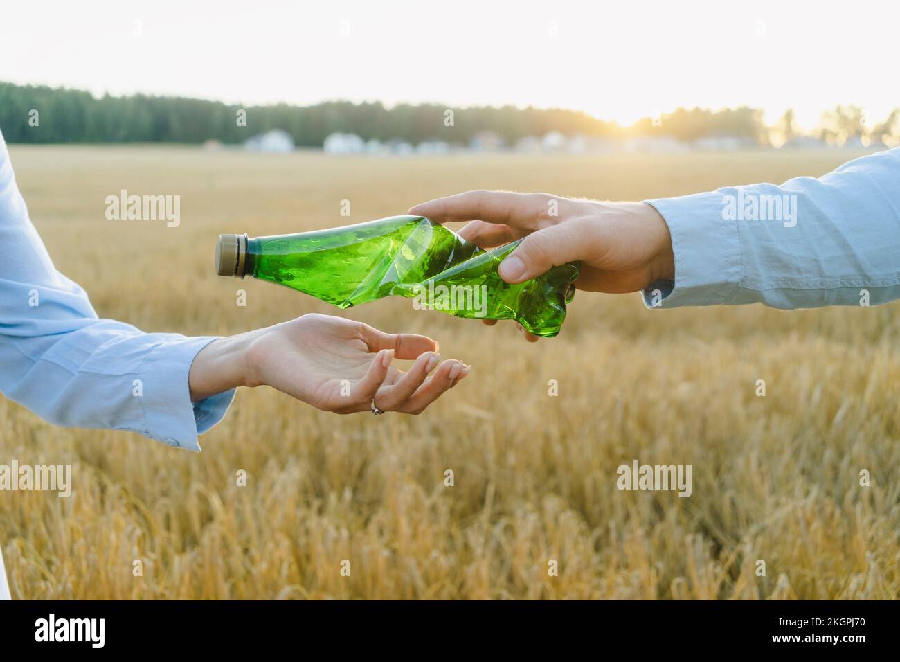 Hand of man passing crumpled plastic bottle to woman at field Stock Photo