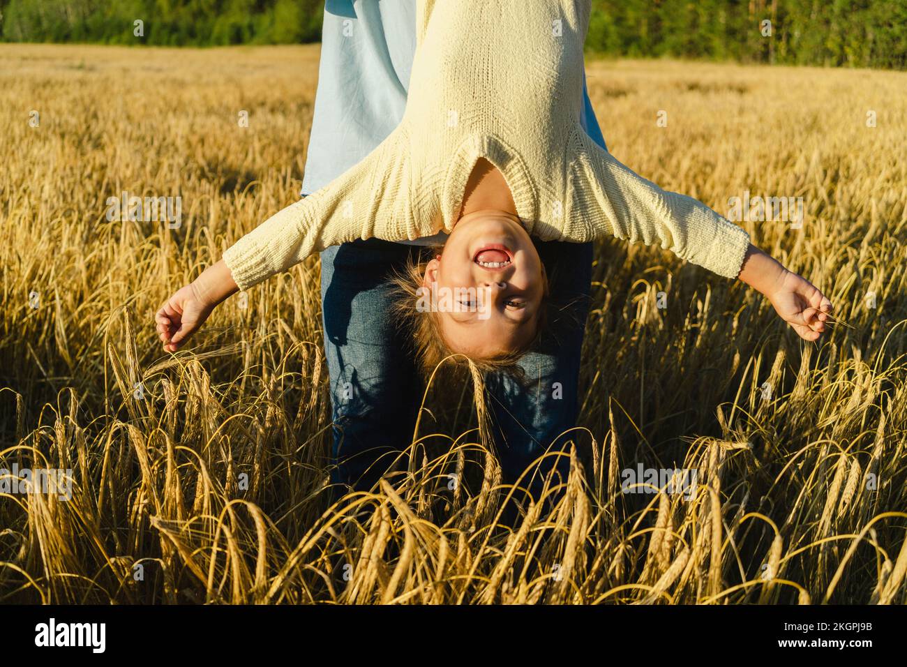 Playful girl with arms outstretched hanging upside down in front of father at field Stock Photo
