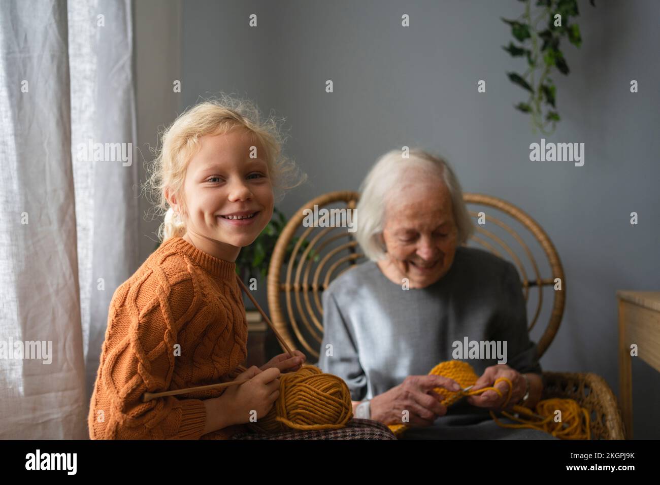 Happy girl holding ball of wool and knitting needle in front of grandmother at home Stock Photo