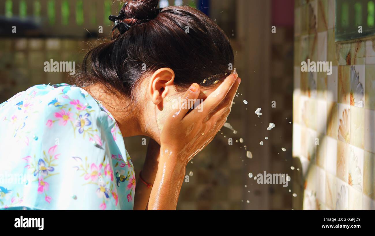 Beautiful woman is washing facial mask in bathroom after applying face mask. Girl spraying water on her face standing in front of mirror at home. mud Stock Photo