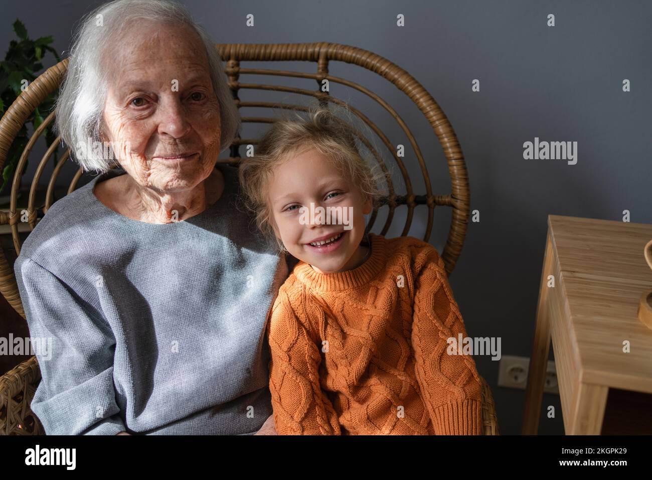 Smiling senior woman with granddaughter on chair at home Stock Photo